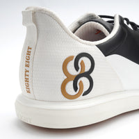 White sneaker with black and gold logo on a white background sells at Paradise Golf