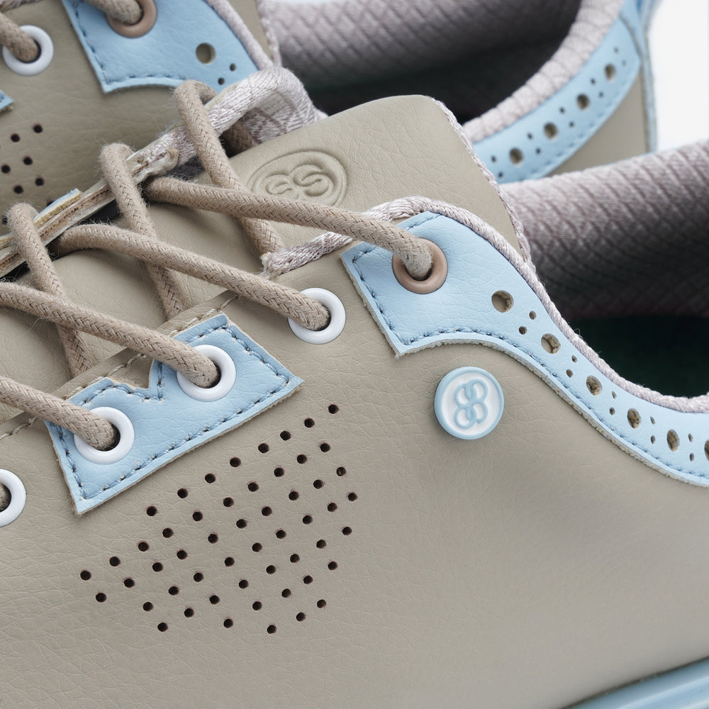 Close-up of a shoe with beige and light blue accents, featuring a brand logo. sells at Paradise Golf