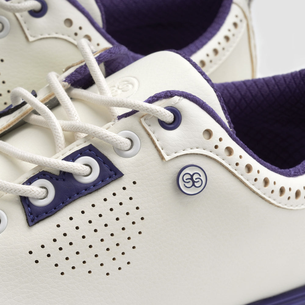 Close-up of a white and purple sneaker with a brand logo on a light background sells at Paradise Golf