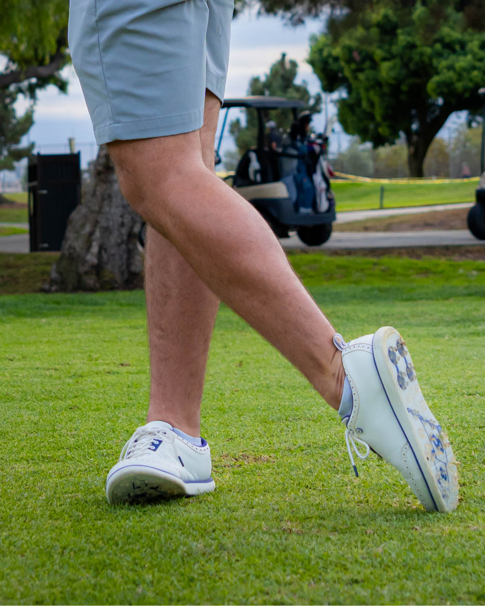 A person playing golf wearing white shoes with blue accents. Sells at Paradise Golf.