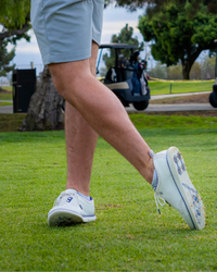A person playing golf wearing white shoes with blue accents. Sells at Paradise Golf.